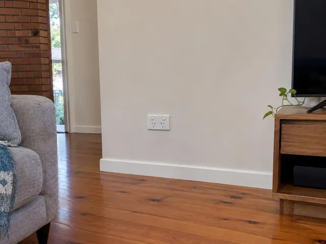 Double power point on a painted living room wall above skirting, beside timber flooring and furniture in Berowra